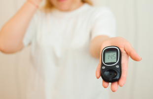 A concerned woman holding a glucose meter with a high blood sugar reading, symbolising the connection between diabetes and mental health.